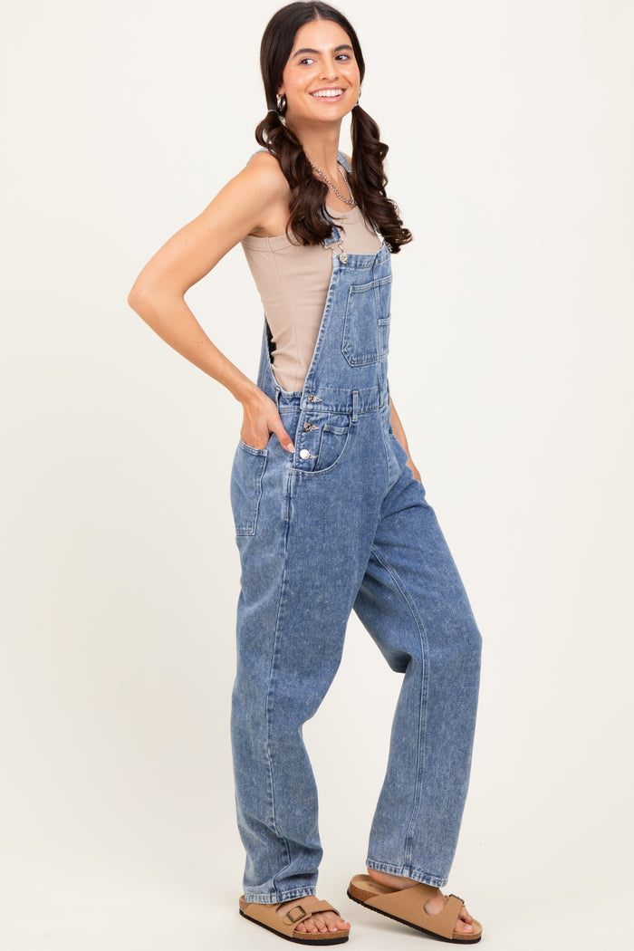 woman wearing a beige tank top and oversized blue denim overalls with pockets