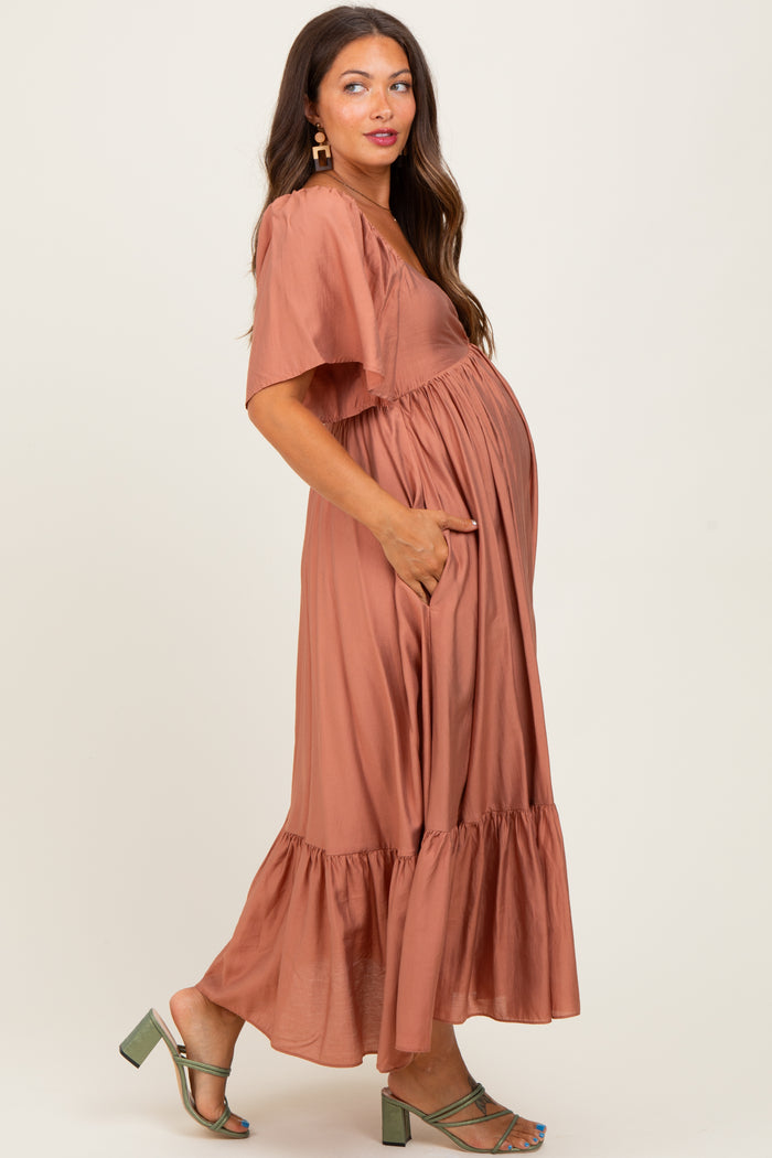 woman wearing a rust-colored maternity maxi dress with short sleeves and a tiered ruffle hem, showcasing her baby bump