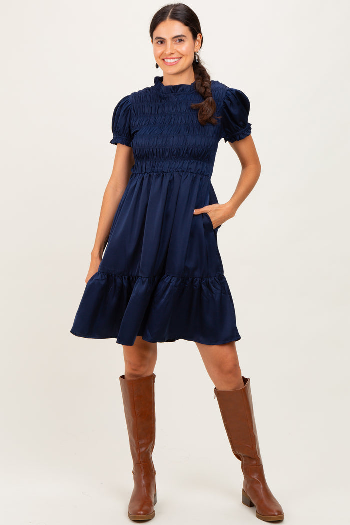 woman wearing a navy blue smocked short sleeve dress with pockets, styled with brown knee-high boots