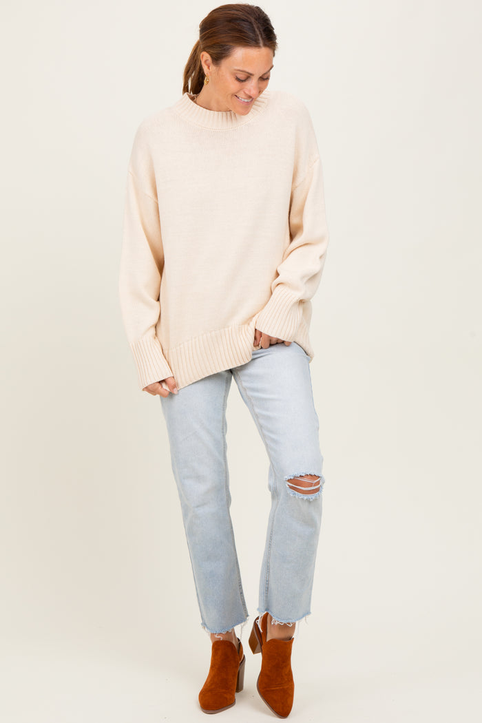 woman wearing a light beige oversized sweater with ribbed details and paired with light blue ripped jeans and brown ankle boots