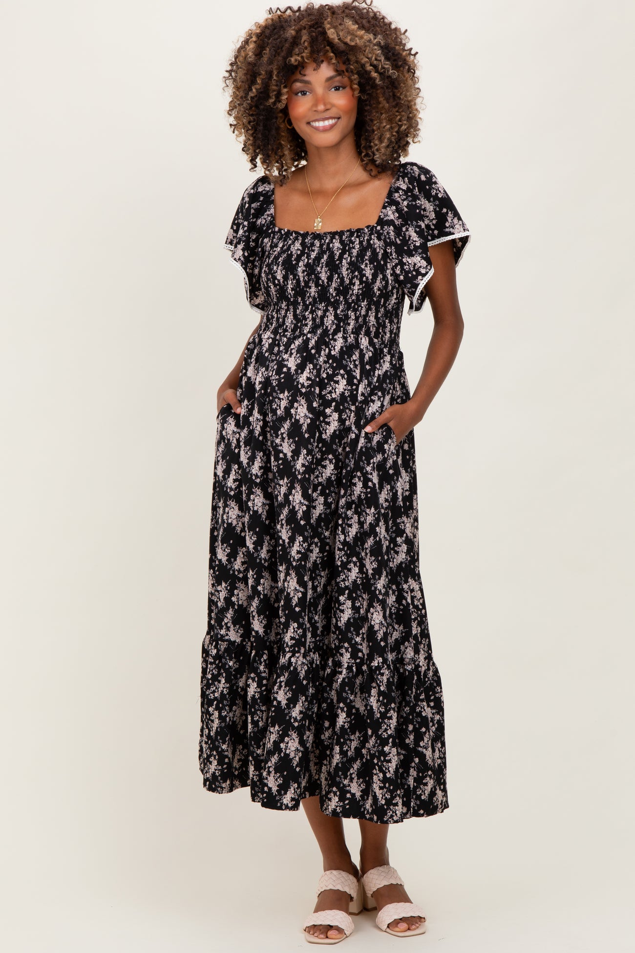 woman wearing a black floral maternity dress with short puff sleeves and pockets, showing her baby bump