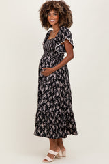 woman wearing a black floral maternity maxi dress and holding her baby bump