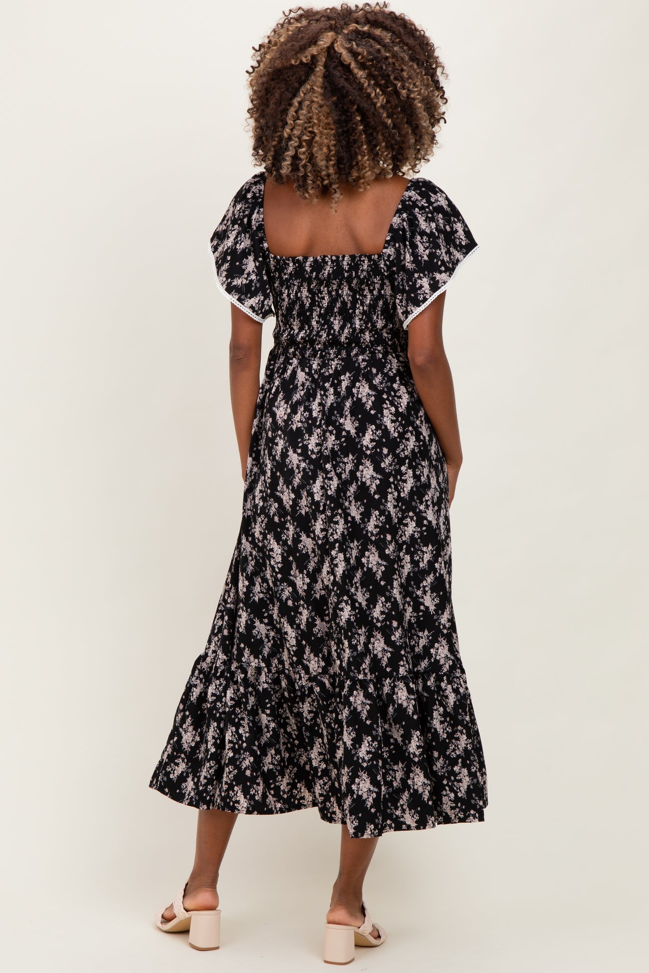 woman wearing a black floral maternity maxi dress with flutter sleeves, showing a fitted bodice and flared skirt
