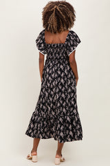 woman wearing a black floral maternity maxi dress with flutter sleeves, showing a fitted bodice and flared skirt