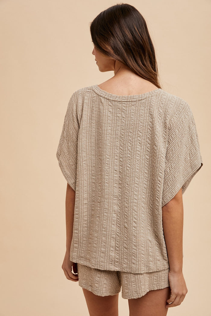woman wearing a beige textured knit short-sleeve top and matching shorts, viewed from the back