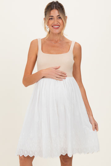 woman wearing a beige ribbed maternity dress with a white embroidered skirt and holding her baby bump
