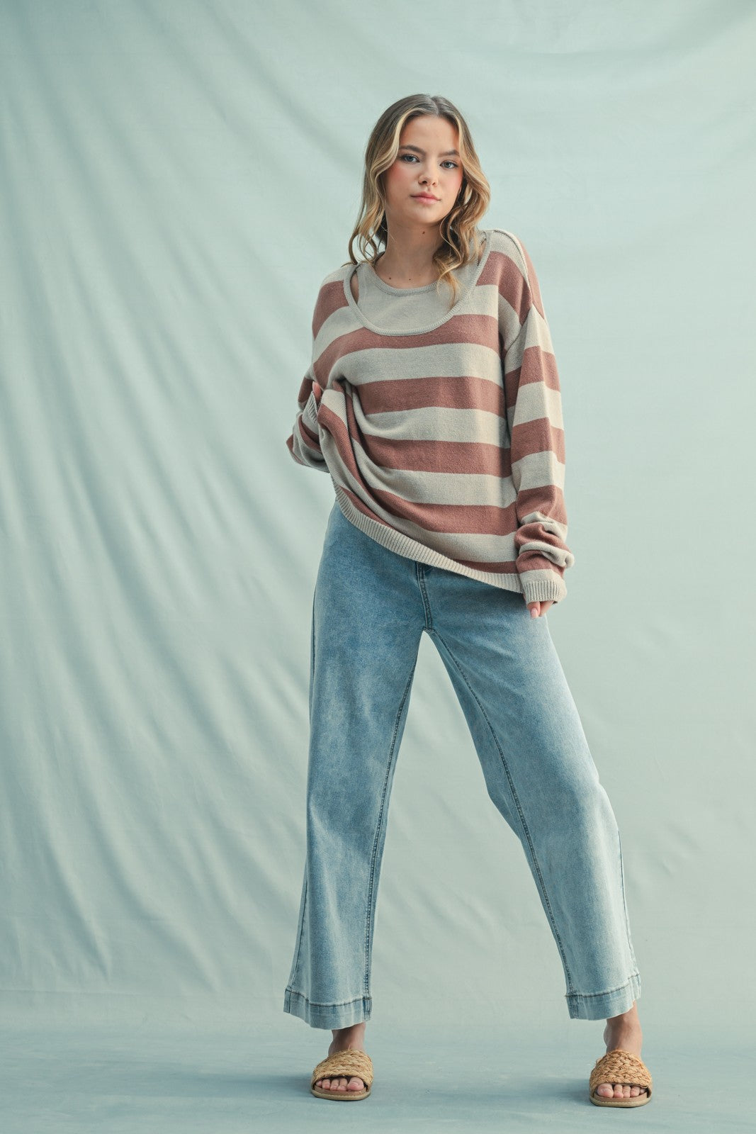 woman wearing a striped beige and brown oversized sweater with light blue wide-leg jeans and tan sandals