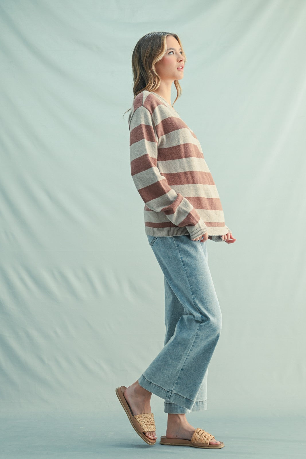 woman wearing a beige and pink striped oversized sweater with light blue wide-leg jeans and flat sandals