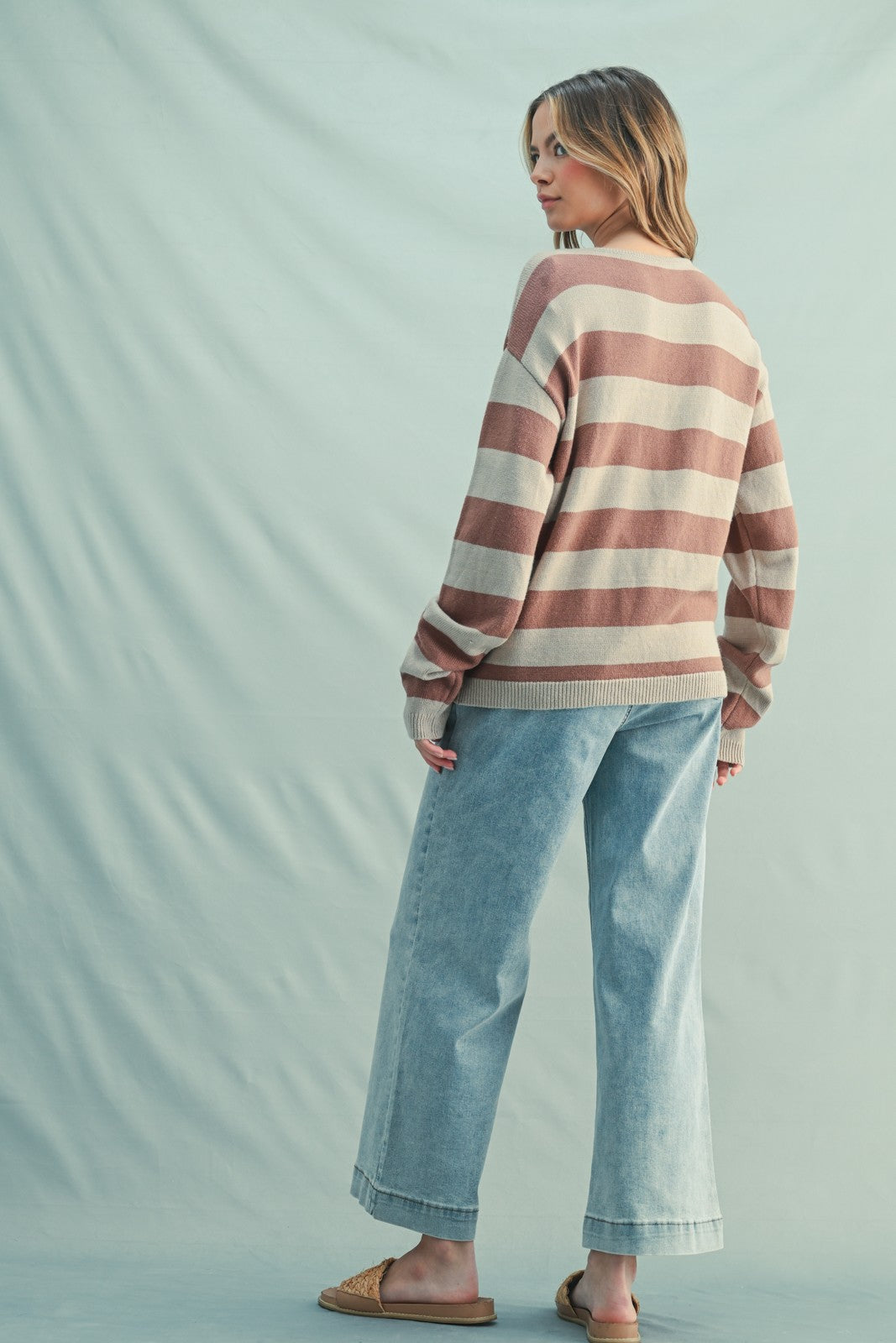 woman wearing a striped sweater in soft pink and cream colors paired with light blue wide-leg jeans