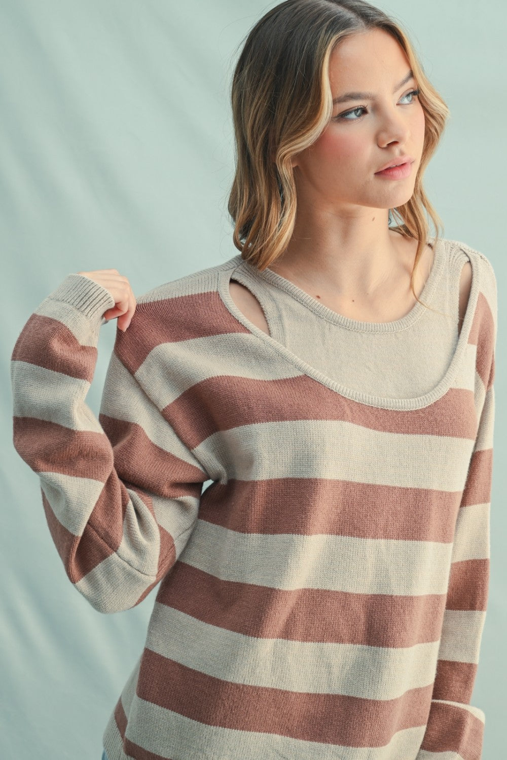 woman wearing a brown and beige striped sweater with cut-out details on the shoulders and layered over a neutral top
