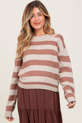 woman wearing a beige and brown striped maternity sweater over a brown tiered dress and smiling, revealing her baby bump