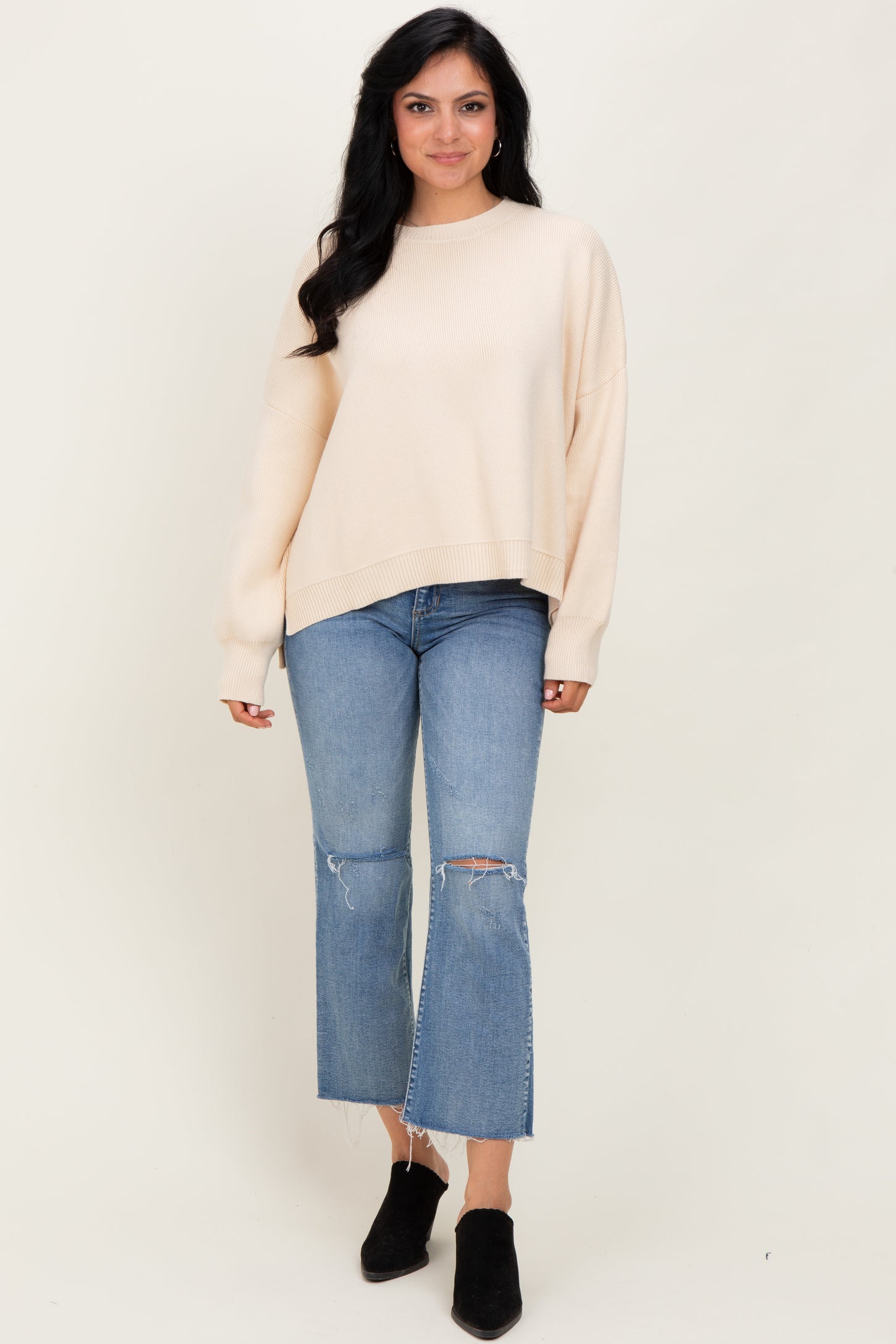 woman wearing a cream oversized knit sweater with distressed light blue cropped jeans and black ankle boots
