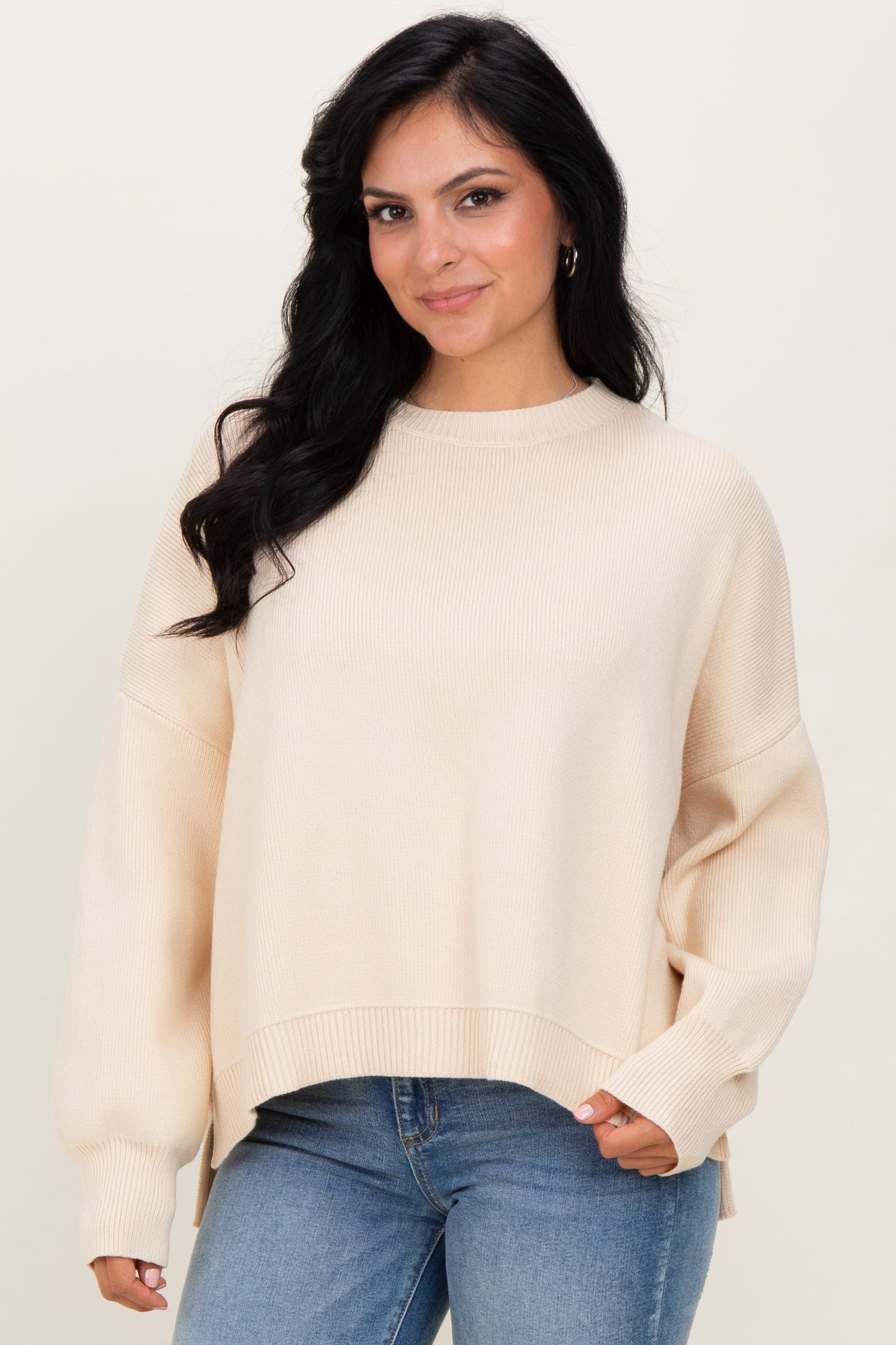 woman wearing a cream oversized sweater with ribbed texture and side slits, paired with blue jeans