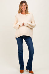 woman wearing a cream oversized maternity sweater and flared blue jeans with a relaxed fit