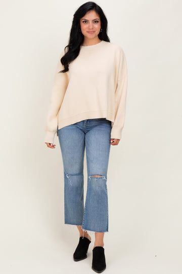 woman wearing a cream oversized knit sweater with distressed light blue cropped jeans and black ankle boots