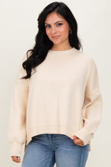 woman wearing a cream oversized sweater with ribbed texture and side slits, paired with blue jeans