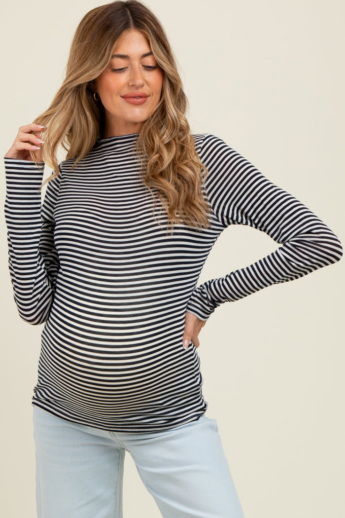 woman wearing a black and white striped maternity top, showing her baby bump, paired with light blue pants