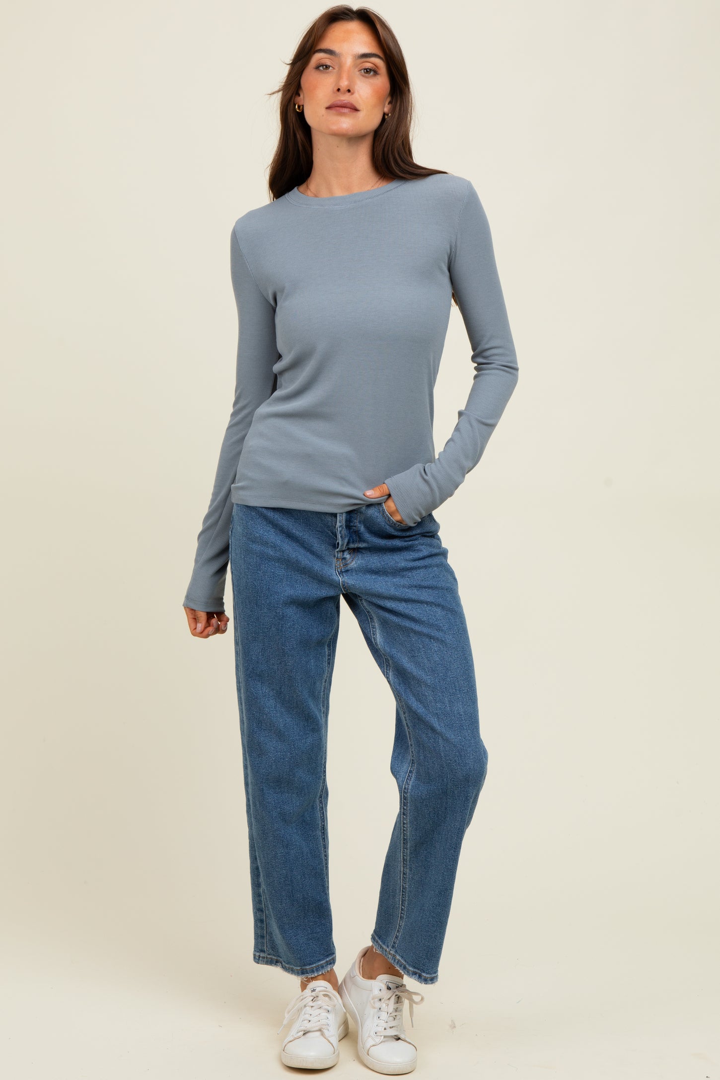 woman wearing a light blue long sleeve ribbed top and high-waisted blue jeans with white sneakers