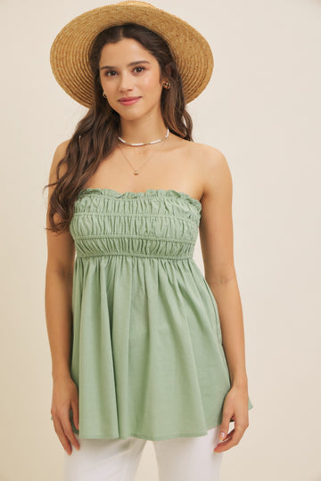 woman wearing a strapless green smocked blouse with a flowy silhouette and a straw hat