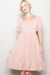 woman wearing a pink and white checkered puff sleeve dress with a smocked bodice and ruffle hem
