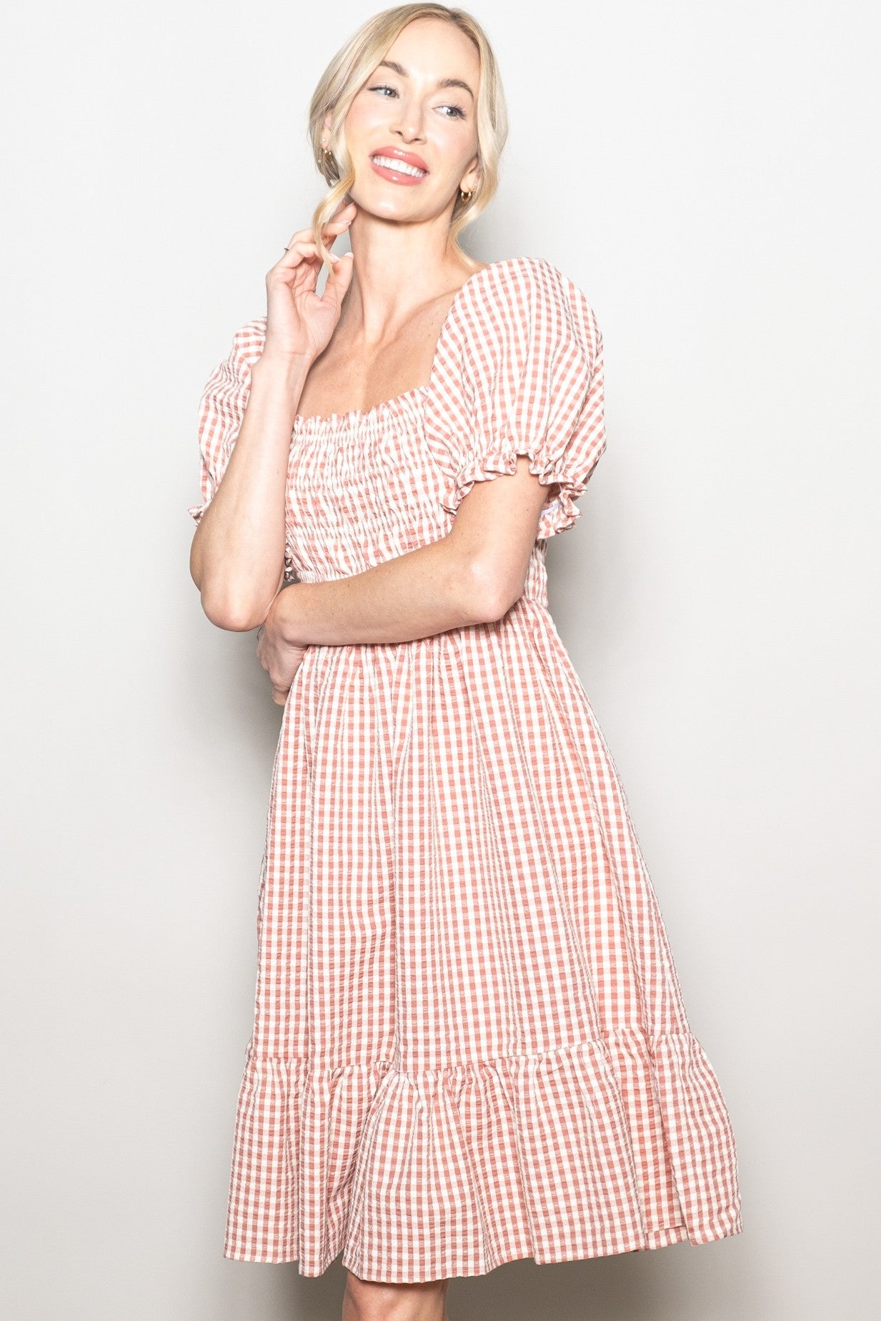 woman wearing a pink and white gingham puff sleeve dress with a square neckline and tiered hem