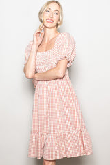 woman wearing a pink and white gingham puff sleeve dress with a square neckline and tiered hem