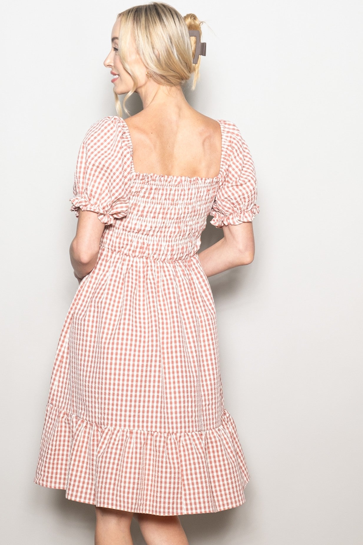 woman wearing a pink and white gingham short sleeve dress with a ruffled hem and smocked back