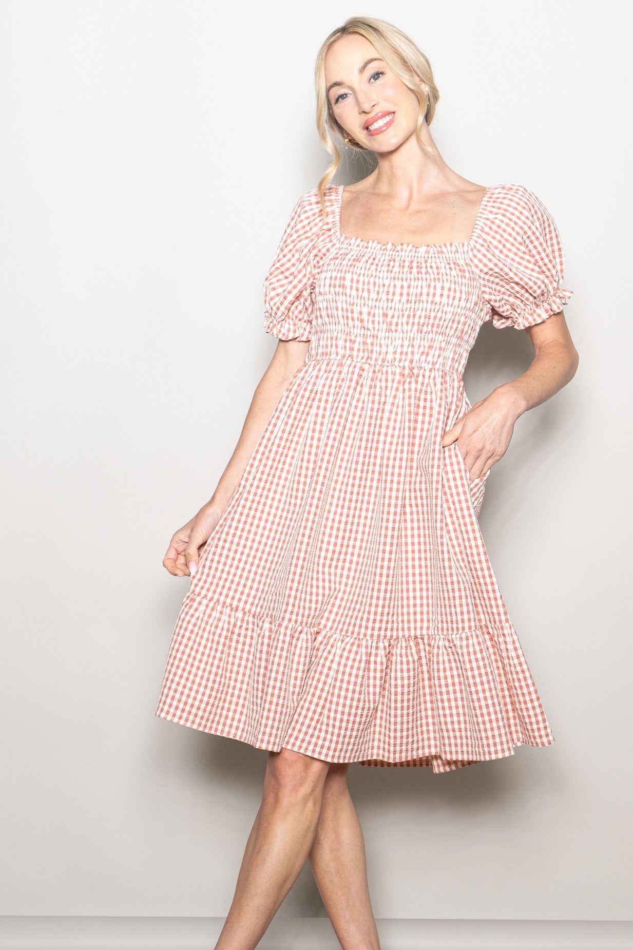 woman wearing a pink and white gingham puff sleeve dress with a smocked bodice and tiered skirt