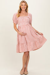 woman wearing a pink and white gingham maternity dress with puff sleeves and a tiered hem, holding her baby bump