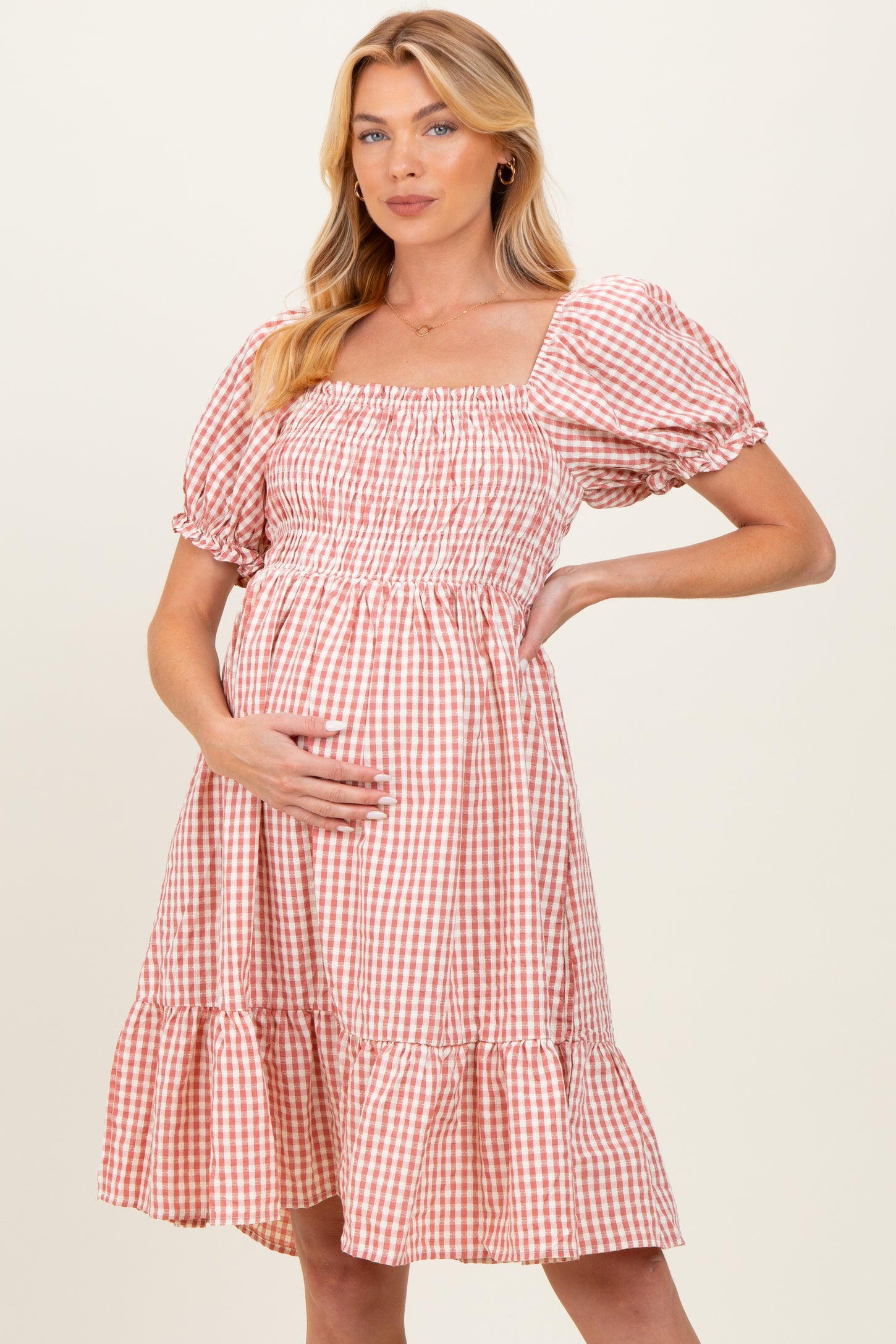 woman wearing a pink and white gingham maternity dress with puff sleeves and a flounced hem, showing her baby bump