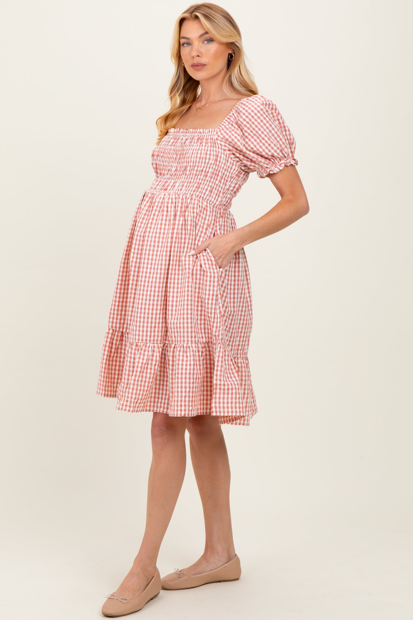 woman wearing a pink and white gingham maternity dress with short puff sleeves and a tiered skirt, showing her baby bump