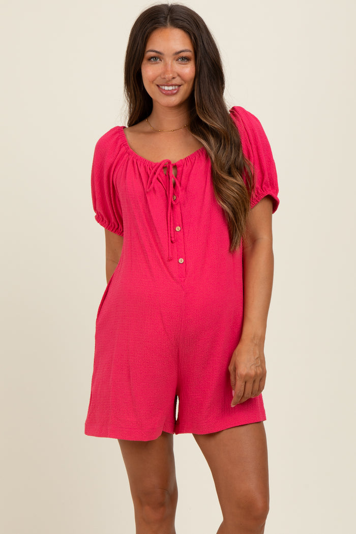 woman wearing a fuchsia short sleeve maternity romper with a tie neckline and buttons