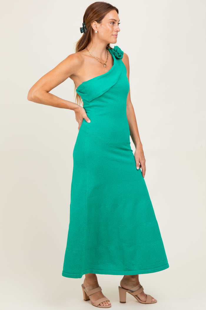woman wearing a green one-shoulder maxi dress with a floral accent, styled with a hair clip and heels