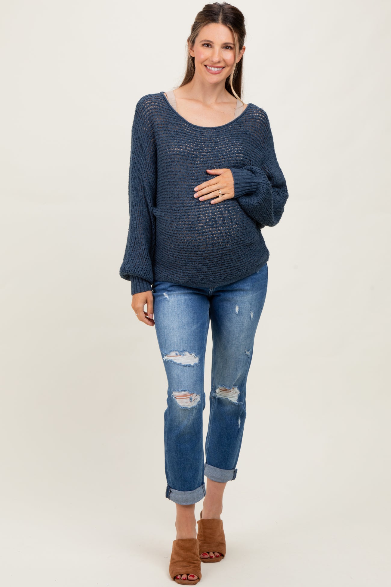 woman wearing a navy blue knitted maternity sweater and distressed jeans, gently cradling her baby bump