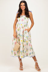 woman wearing a floral maxi dress with ruffled straps and pockets, holding a small woven bag