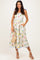 woman wearing a floral maxi dress with ruffled straps and pockets, holding a small woven bag