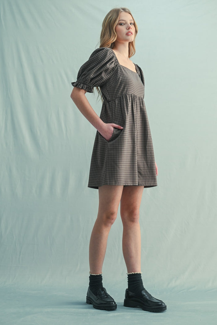 woman wearing a brown checkered short dress with puff sleeves and pockets, standing on a light background