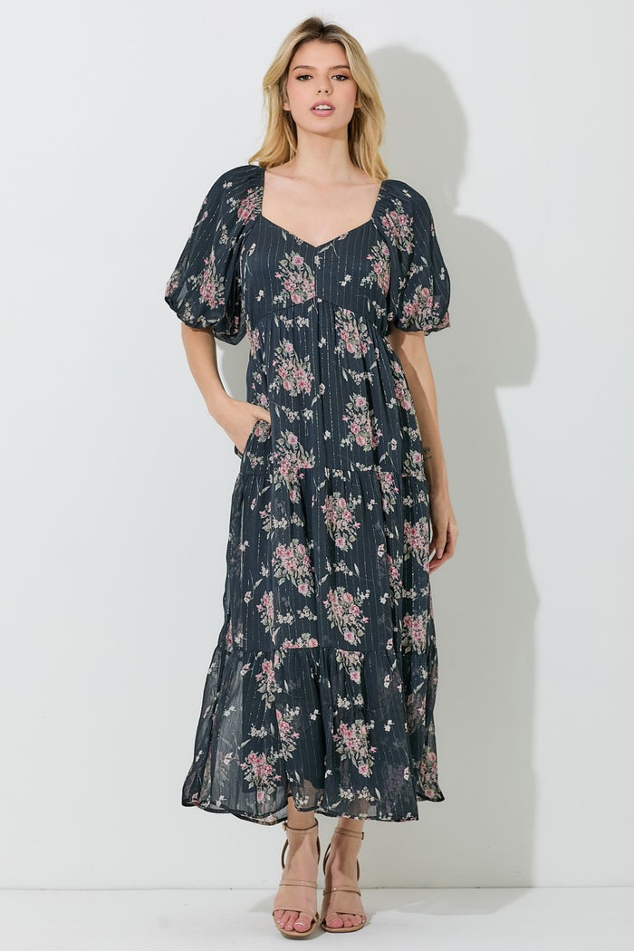 woman wearing a navy floral maxi dress with puff sleeves and pockets, standing against a light backdrop