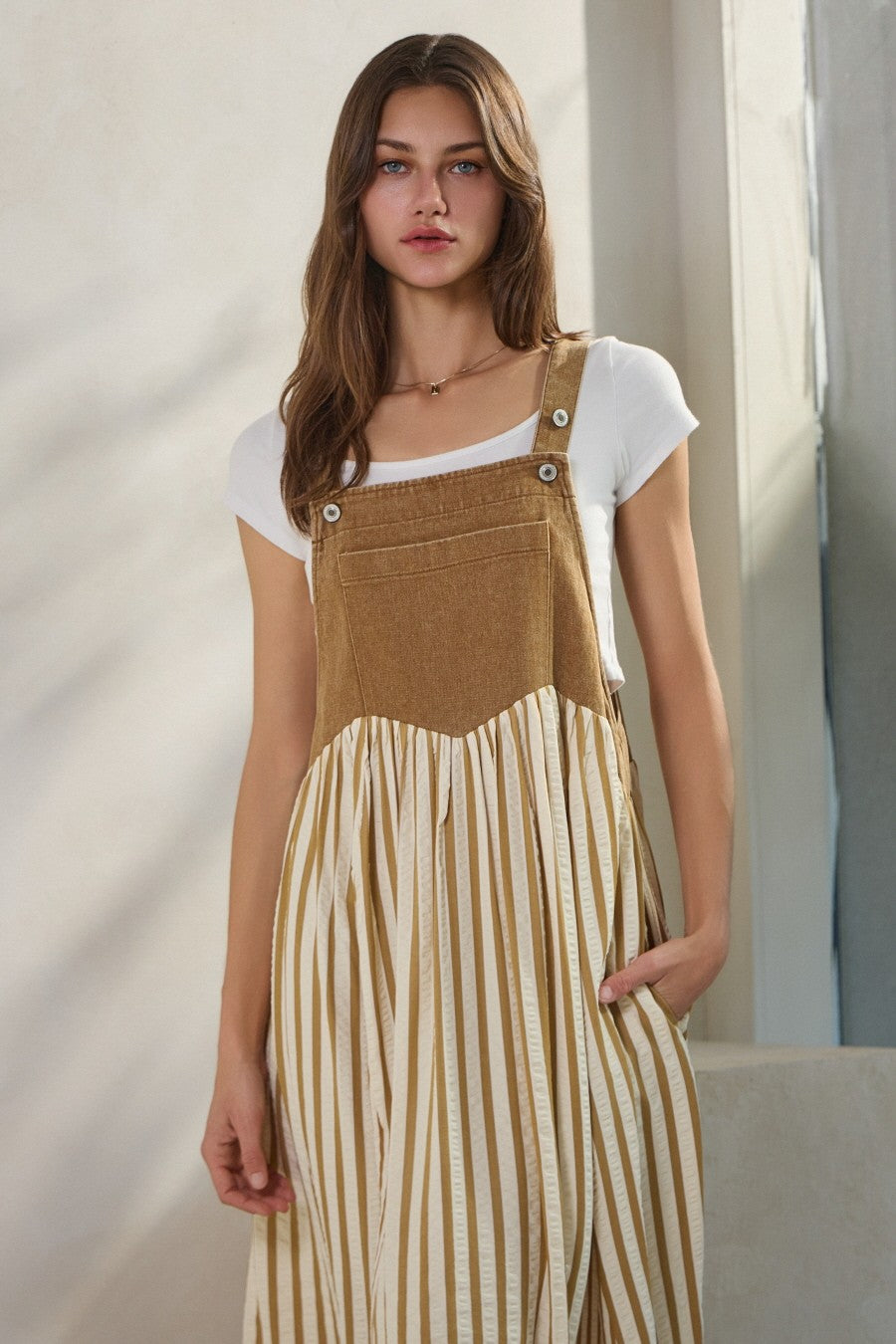 woman wearing a tan corduroy and striped long dress with buttons and pockets over a white t-shirt
