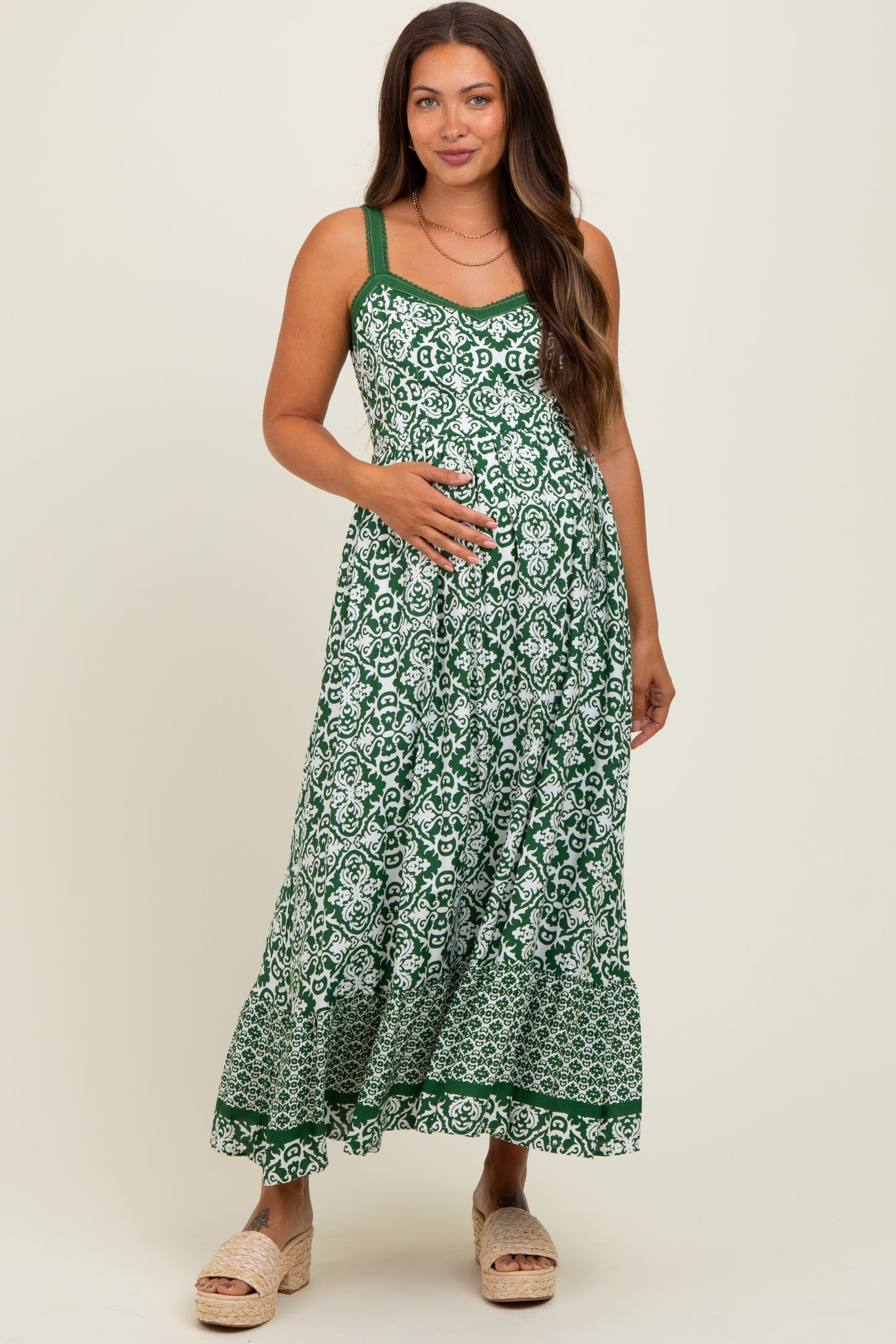 woman wearing a green and white floral maternity maxi dress and gently holding her baby bump