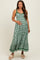 woman wearing a green and white floral maternity maxi dress and gently holding her baby bump