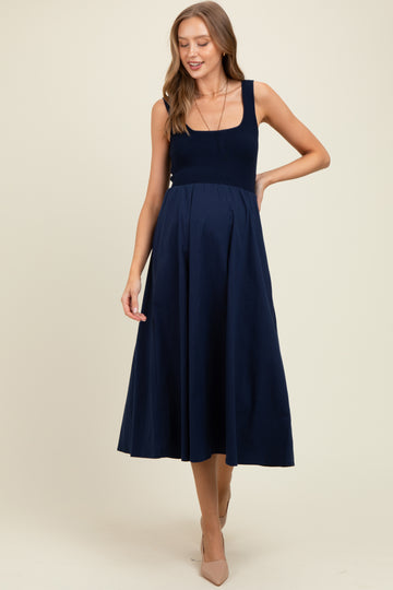 woman wearing a navy blue sleeveless maternity dress with a square neckline and a flowy skirt, showing her baby bump