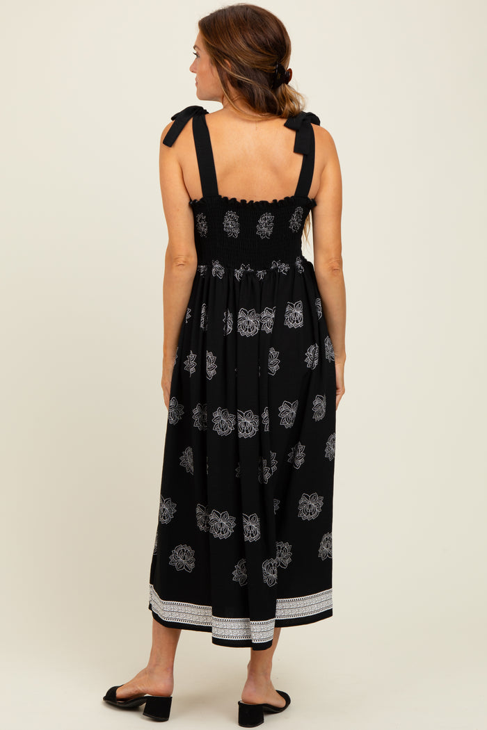 woman wearing a black maxi dress with floral pattern and tie shoulder straps, shown from the back