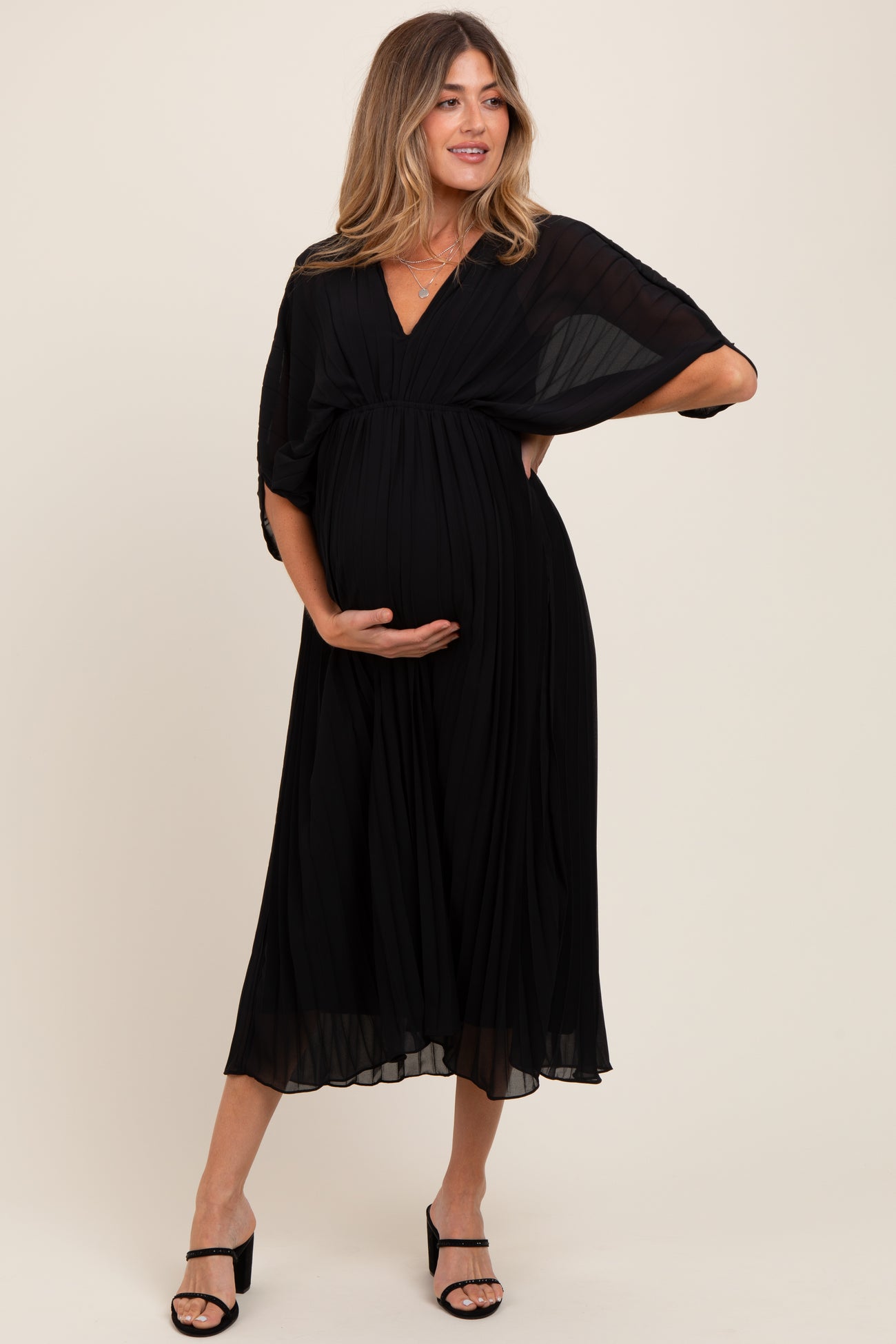 woman wearing a black pleated maternity dress with a deep v-neckline and flutter sleeves, showcasing her baby bump