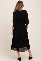 woman wearing a black pleated maternity dress with a flowing silhouette, showing a gathered waist and ankle length