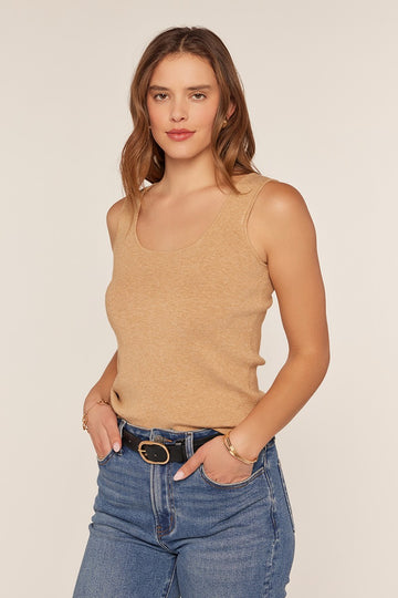 woman wearing a tan sleeveless knit top paired with high-waisted blue jeans, standing with hands on hips