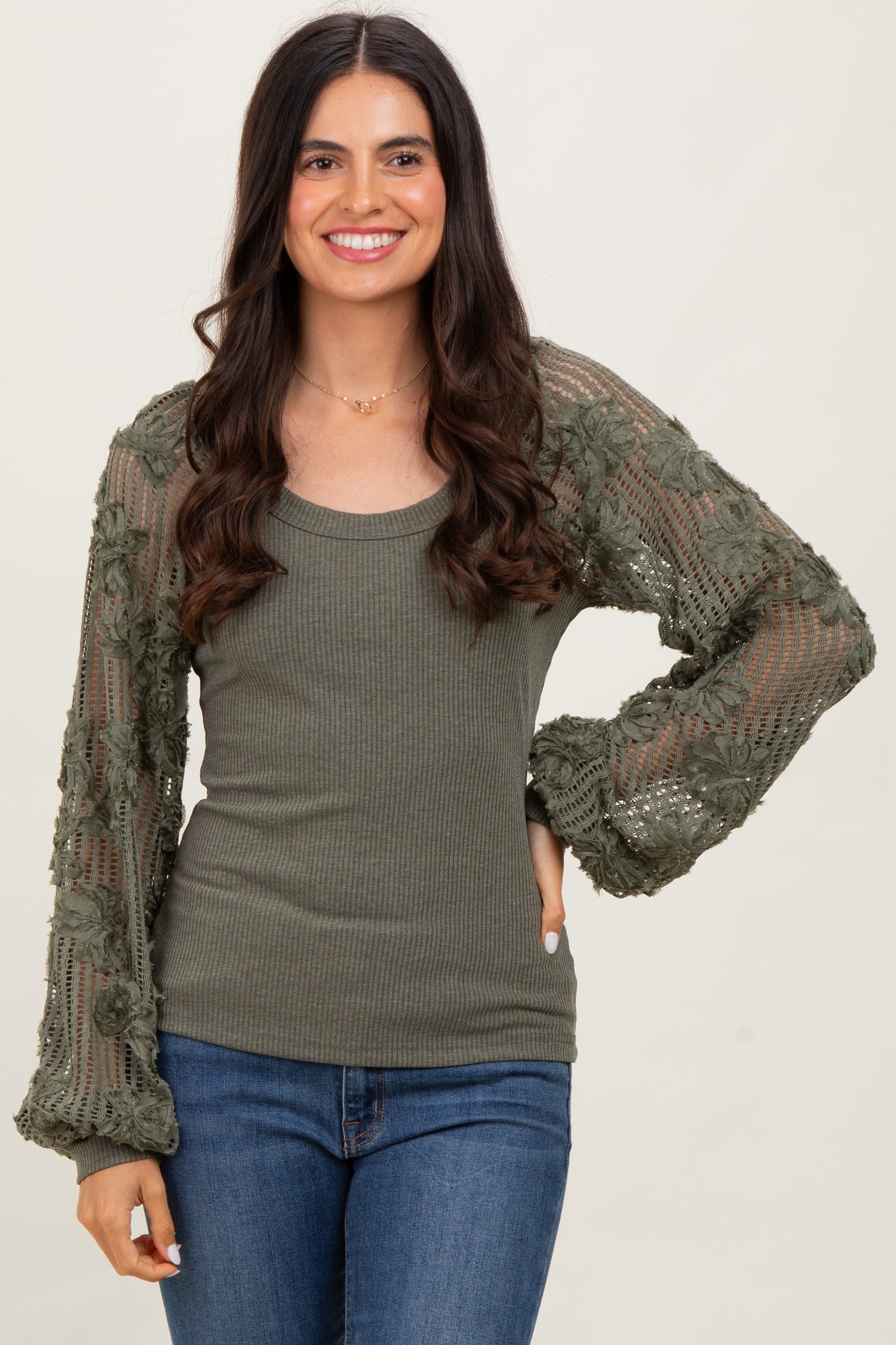 woman wearing an olive green ribbed top with lace sleeves and a relaxed fit, smiling against a neutral background