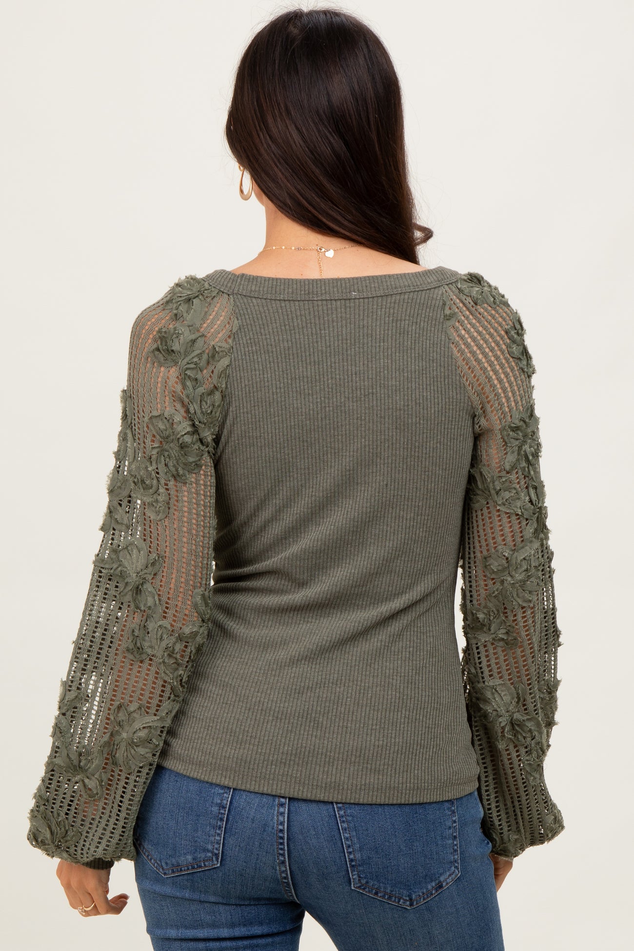woman wearing an olive green ribbed top with floral mesh long sleeves and fitted style, seen from the back