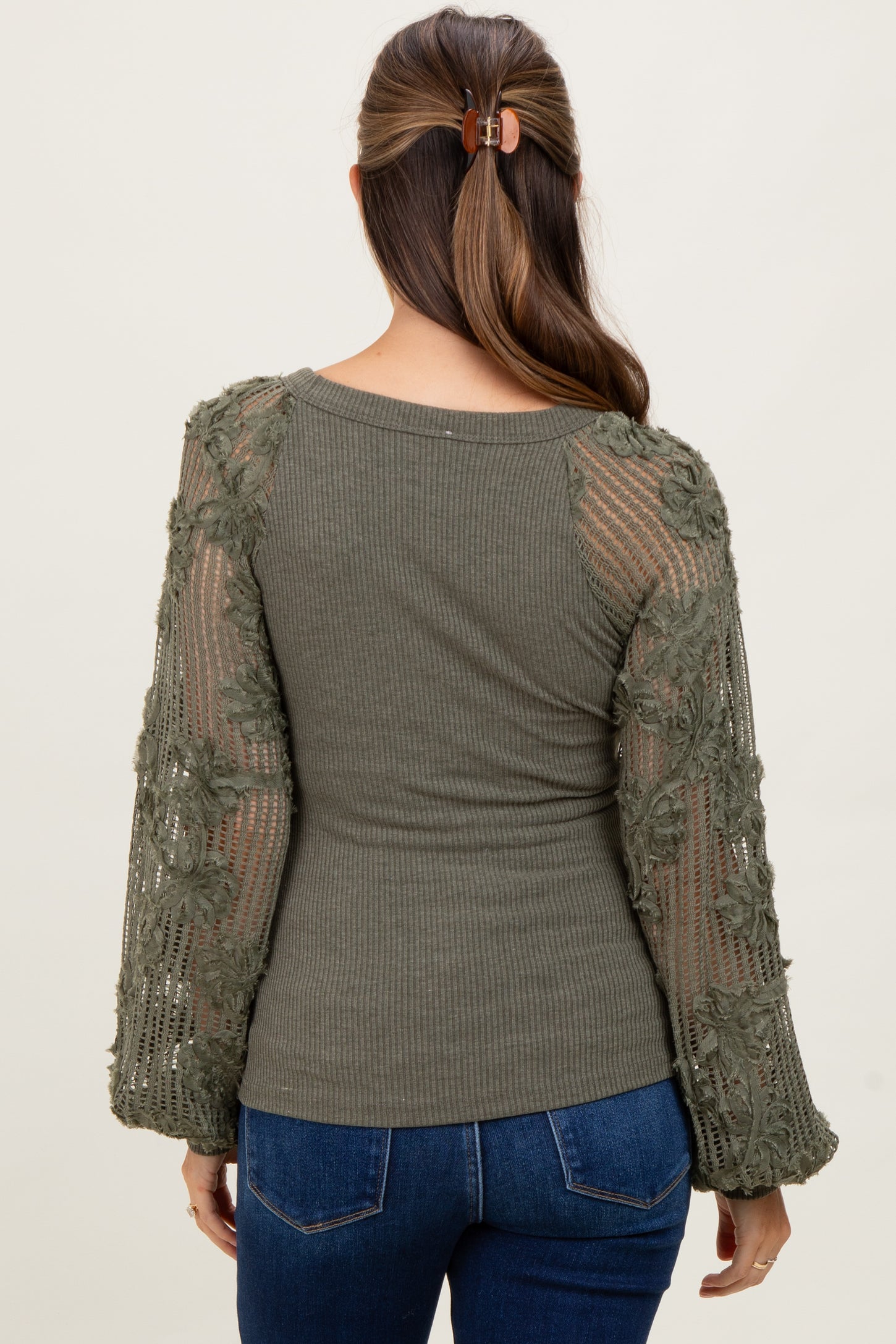 woman wearing a green maternity top with floral lace sleeves, showing her pregnant belly from the back