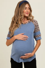 woman wearing a blue ribbed maternity top with leopard print sleeves and holding her baby bump